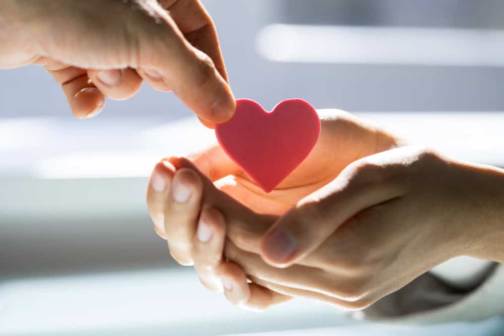 Hands exchanging a red heart symbolizing love, generosity, and charitable giving inspired by biblical stewardship.